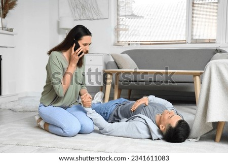 Young woman calling ambulance while her husband having heart attack at home Royalty-Free Stock Photo #2341611083