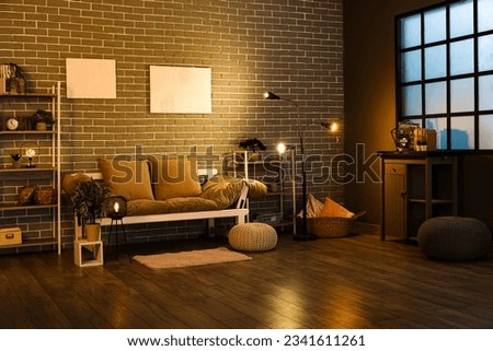 Interior of dark living room with couch, shelving units and glowing lamps Royalty-Free Stock Photo #2341611261