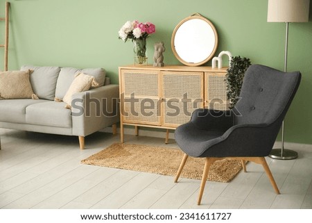 Armchair with dresser, couch and lamp near green wall