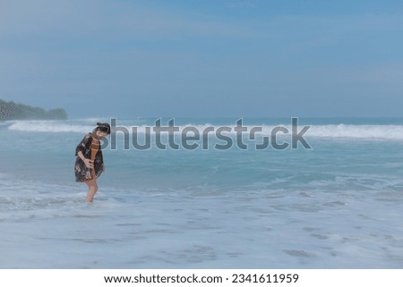 Lonely young woman enjoying the waves crashing against her on the blue beach