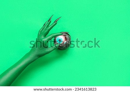 Hand of witch with cauldron and eye on green background. Halloween celebration