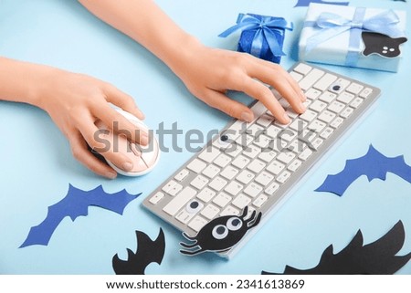 Female hands with modern computer keyboard, mouse, gift boxes and paper bats for Halloween on blue background, closeup