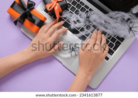 Female hands with modern laptop, gift boxes for Halloween on purple background, closeup