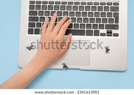 Female hand with modern laptop and spiders for Halloween on blue background
