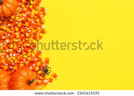 Tasty Halloween candy corns, pumpkins and spider on yellow background