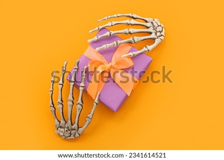 Skeleton hands with gift box for Halloween on orange background