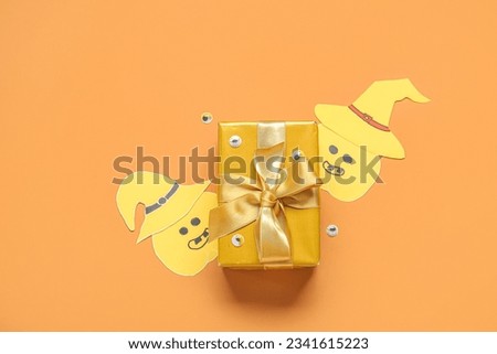Composition with beautiful gift box and Halloween decor on orange background