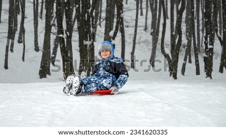 Young boy sledging down a snowy hill with excitement and exhilaration. The perfect scene to showcase the fun and joy of winter playtime during the holiday season