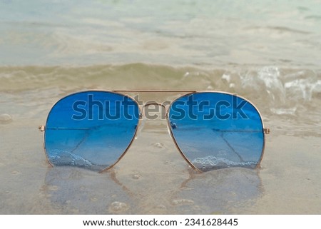 Blue sunglasses lie in the sand on the beach near the sea. Summer vacation, travel and tourism concept. Summer rest. Vacation season.