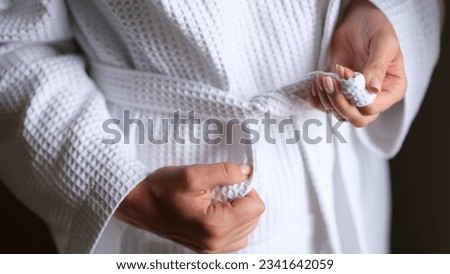 Natural fabric and closeup of female hands tying belt of white robe Royalty-Free Stock Photo #2341642059