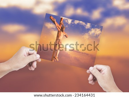 Human hands holding picture Jesus christ on the cross over a sunset background.