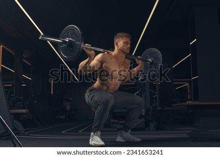 Muscular man doing squats with barbell in a gym. Male bodybuilder doing workout Confident young man doing barbell workout in gym Powerful attractive man. Royalty-Free Stock Photo #2341653241