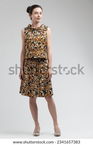 Classic fashion model pose, relaxed, in a 70's patterned dress with mid-heeled shoes. Full-length portrait against a neutral background, she has very long hair, light eyes and complexion, possibly Nor