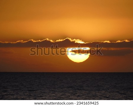 Extreme zoom photo of subtropical summer sunset with sun partly hidden by 
clouds with beautiful golden colours Royalty-Free Stock Photo #2341659425