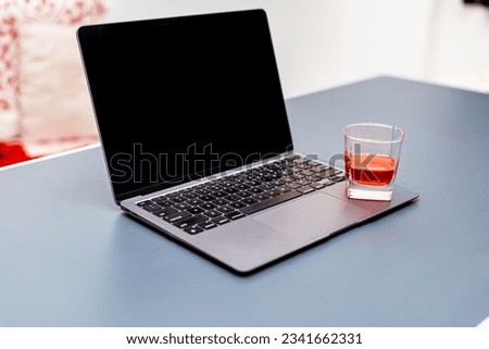 A glass of red wine sits on top of a laptop computer. The laptop is open