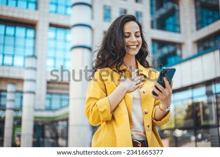 Woman using smartphone and drinking coffee at the city. Closeup shot of a businesswoman using a cellphone in the city. Young smiling woman holding a smartphone and a cup of coffee looking at device  Royalty-Free Stock Photo #2341665377