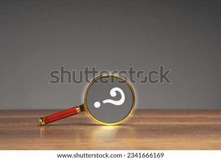 A magnifying glass with a question mark on a wooden table against a gray background. Space for text. Royalty-Free Stock Photo #2341666169