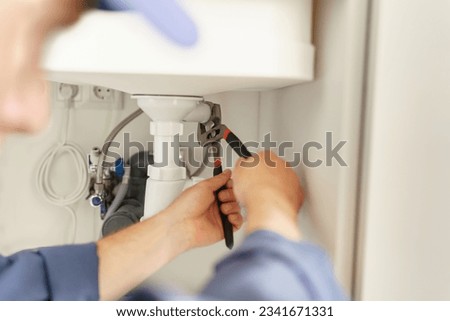 Close up of professional plumber repairing a siphon pipe with adjustable wrench on the kitchen Royalty-Free Stock Photo #2341671331