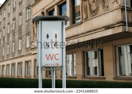 WC logo, sign of public toilets in the street against building background. For female, male and disabled people.