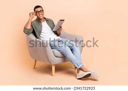 Full length photo of cool dreamy guy dressed khaki shirt siting chair reading modern device empty space isolated beige color background