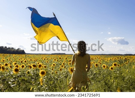 Ukrainian flag in hands of woman standing with back on flowering field of sunflowers. National symbol of freedom and independence. stop the war. hope and faith in victory. Rear view, backlight