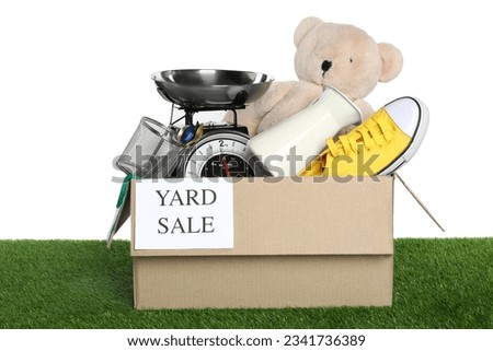 Sign Yard Sale written on box with different stuff on green grass against white background