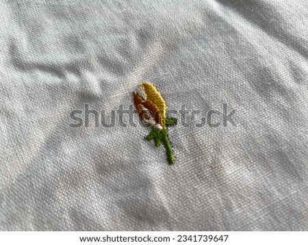 Closeup of hand embroidered flower butti with yellow silk thread on white cotton fabric 