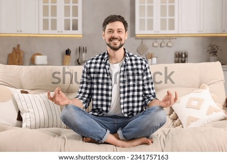 Happy man meditating on sofa at home. Harmony and zen