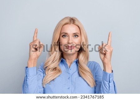 Photo of confident mature lady wear blue shirt pointing fingers up empty space information message isolated on grey color background