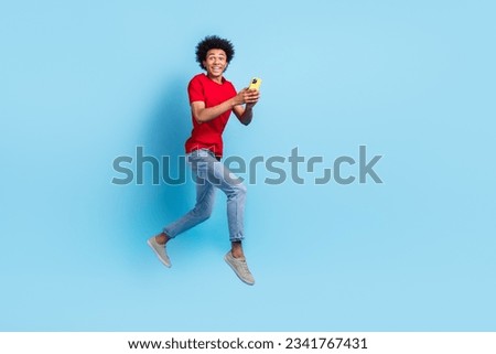Full size photo of cheerful guy dressed red stylish t-shirt denim pants typing email on smartphone isolated on blue color background