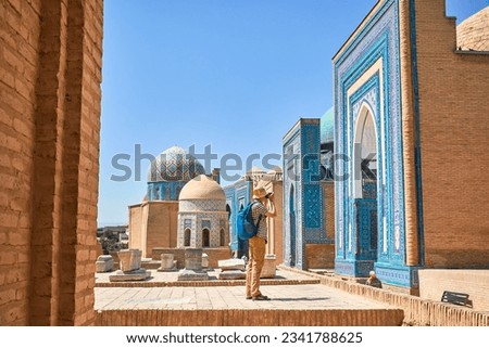 Tourist with photo camera in Beautiful Historical cemetery of Shahi Zinda entry Gate with finely decorated by blue and turquoise stone mosaic mausoleums in Samarkand, Uzbekistan.