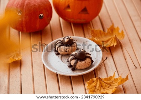Cute funny spiders cookies with Halloween pumpkin among fall leaves. Trick or treat. Handmade cookies
