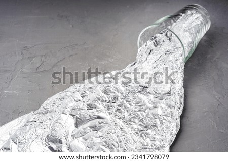 the foil symbolizes water flowing out of a glass glass on a gray surface. art object foil from a glass