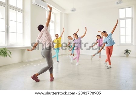 Group of kids having dance class. Woman teacher teaches girls ballet like movements. Children dancers rehearsing new choreography in spacious, light, white room at modern gym or dance school