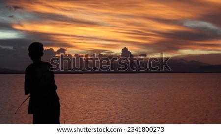 silhouette of a fisherman with a fishing rod in the lake at sunset
