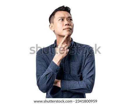 A portrait of an Asian man wearing a blue shirt,  looking confused and pointing his hand to touch his chin. Isolated with a white background.