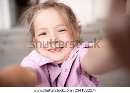 Cute kid girl 4-5 year old making selfie or taking video on phone. Looking at camera. Childhood. 