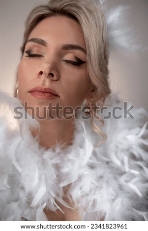 Portrait of a beautiful bride with a wedding hairstyle dressed in a white dress with feathers. A girl with a professional makeup against the wall Royalty-Free Stock Photo #2341823961