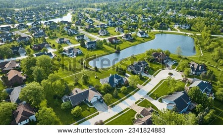 Houses around small neighborhood pond with variety of homes in summertime aerial