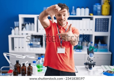 Young hispanic man working at scientist laboratory smiling making frame with hands and fingers with happy face. creativity and photography concept. 