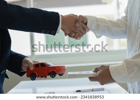 
image of men holding hands with a red car after signing the contract and paying successfully The car dealer or sales manager offers to sell the car and explains the terms of the car contract and insu