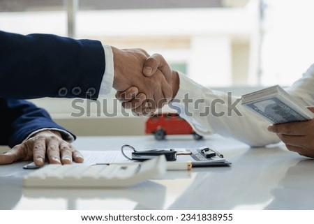 
image of men holding hands with a red car after signing the contract and paying successfully The car dealer or sales manager offers to sell the car and explains the terms of the car contract and insu
