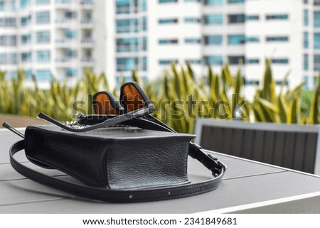 Black stylish glasses and a black bag on the table. Expensive clothing accessories outside in a cafe