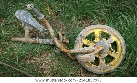 A broken dirty children's bicycle lies on the grass near a residential building in the city, color photograph.