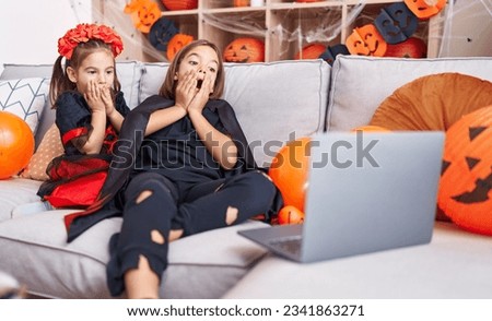 Adorable boy and girl wearing halloween costume watching movie on laptop with terrified expression at home