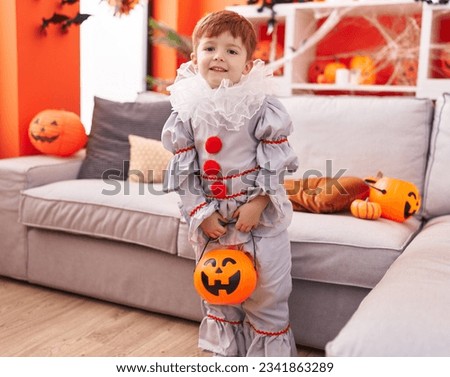 Adorable toddler wearing harlequin costume holding pumpkin basket at home