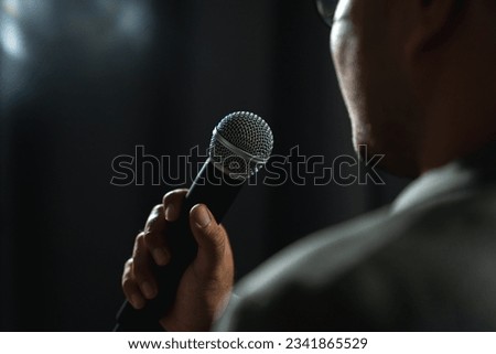 Confident successful speaker man talking on stage with spotlight strike through the darkness at corporate business event. Public speaker giving talk at conference hall. Stand up comedian. Royalty-Free Stock Photo #2341865529