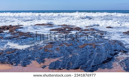 Beach rocky coastline waters edge towards blue ocean waves and horizon blue sky landscape.