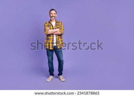 Full size photo of friendly nice man wear yellow plaid shirt denim trousers standing arms crossed isolated on purple color background