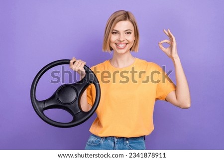 Photo of cheerful girl with bob hairstyle dressed yellow t-shirt hold steering wheel show okey good job isolated on violet background